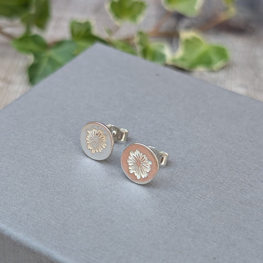 silver daisy stud earrings displayed on a grey jewellery box, showing the round shape, stamped daisy design and butterfly backs.
