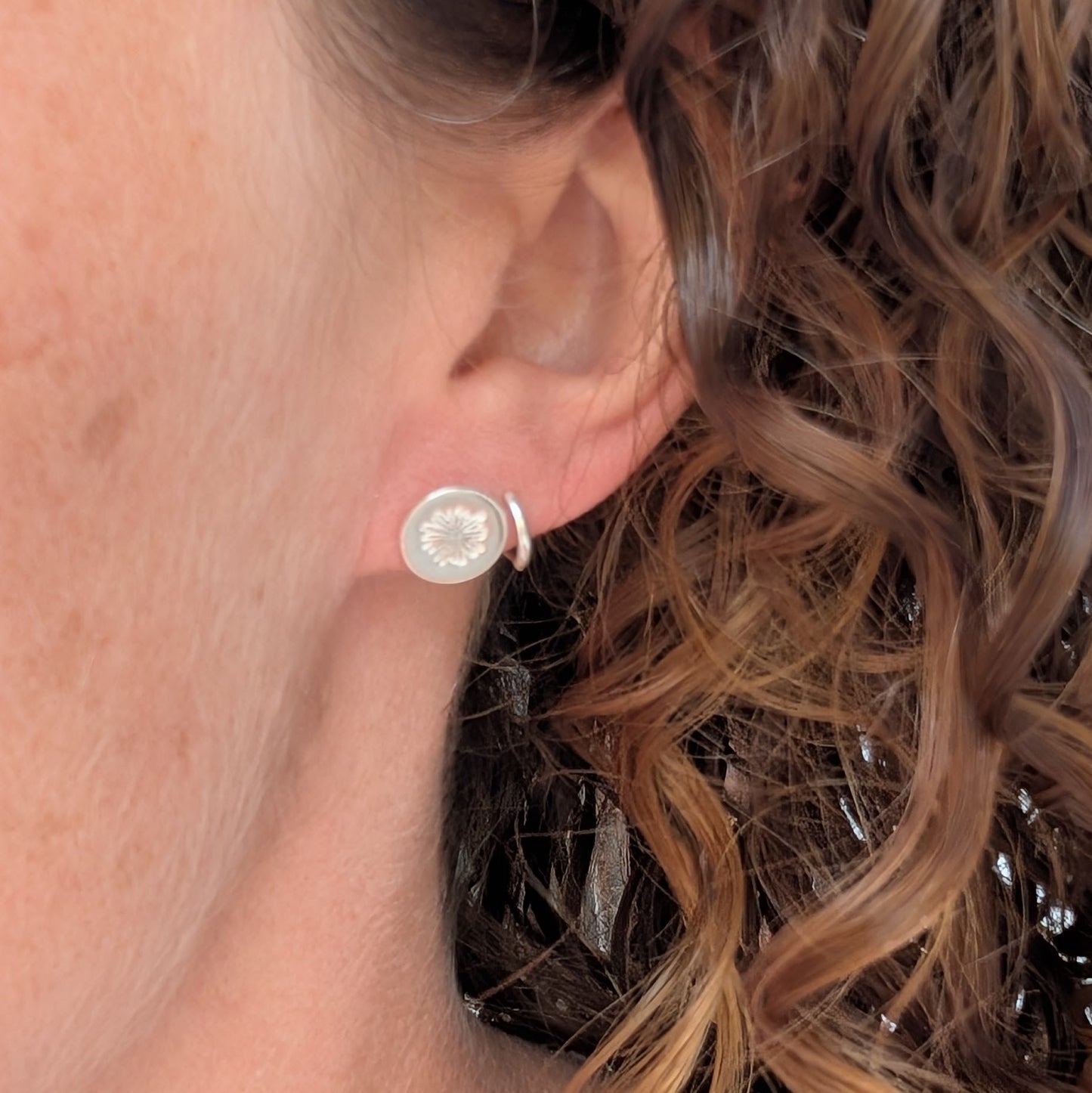 silver daisy stud earrings being worn in the ear, showing the size and simple round floral design.