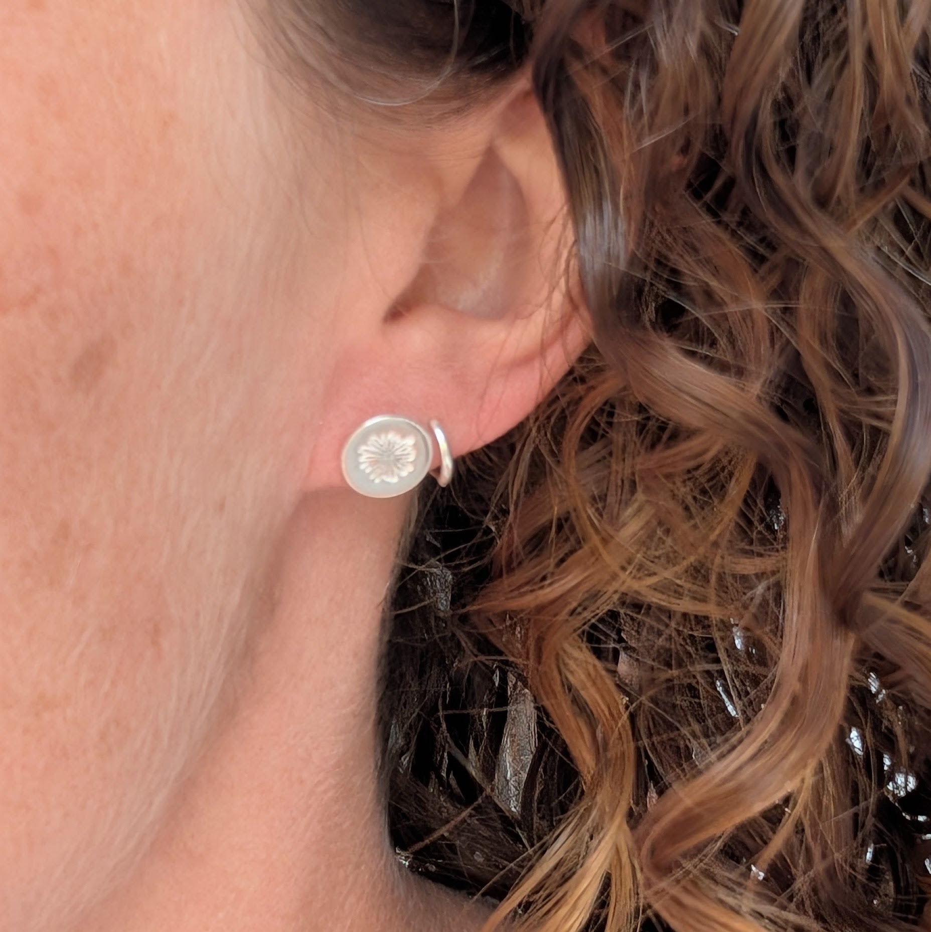 silver daisy stud earrings being worn in the ear, showing the size and simple round floral design.