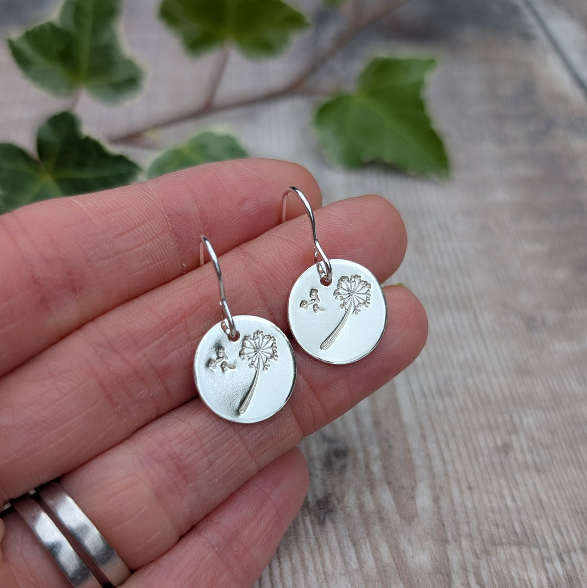 Silver dandelion and wishes disc earrings held in a hand, showing the recycled Sterling Silver discs and stamped dandelion design.