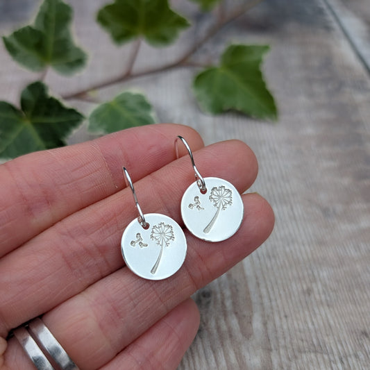 Silver dandelion and wishes disc earrings handmade from recycled Sterling Silver, held in a hand showing the stamped dandelion design.