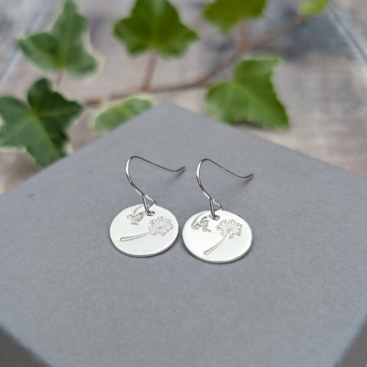 Close up of silver dandelion and wishes disc earrings showing the hand stamped dandelion and floating seed pattern.