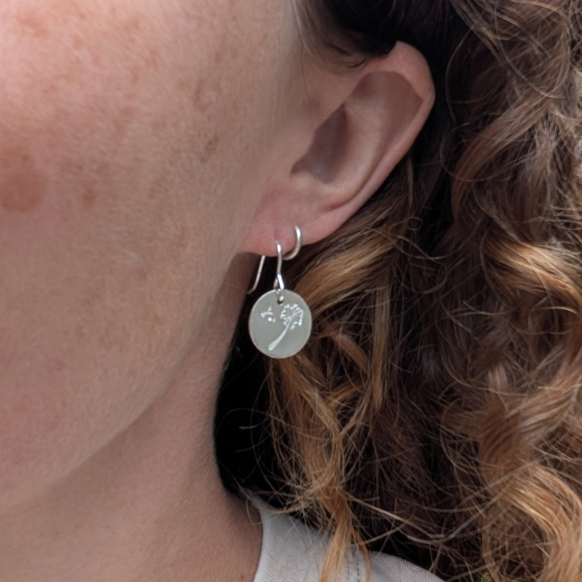 Silver dandelion and wishes disc earrings being worn, showing the size and drop of the round silver discs.