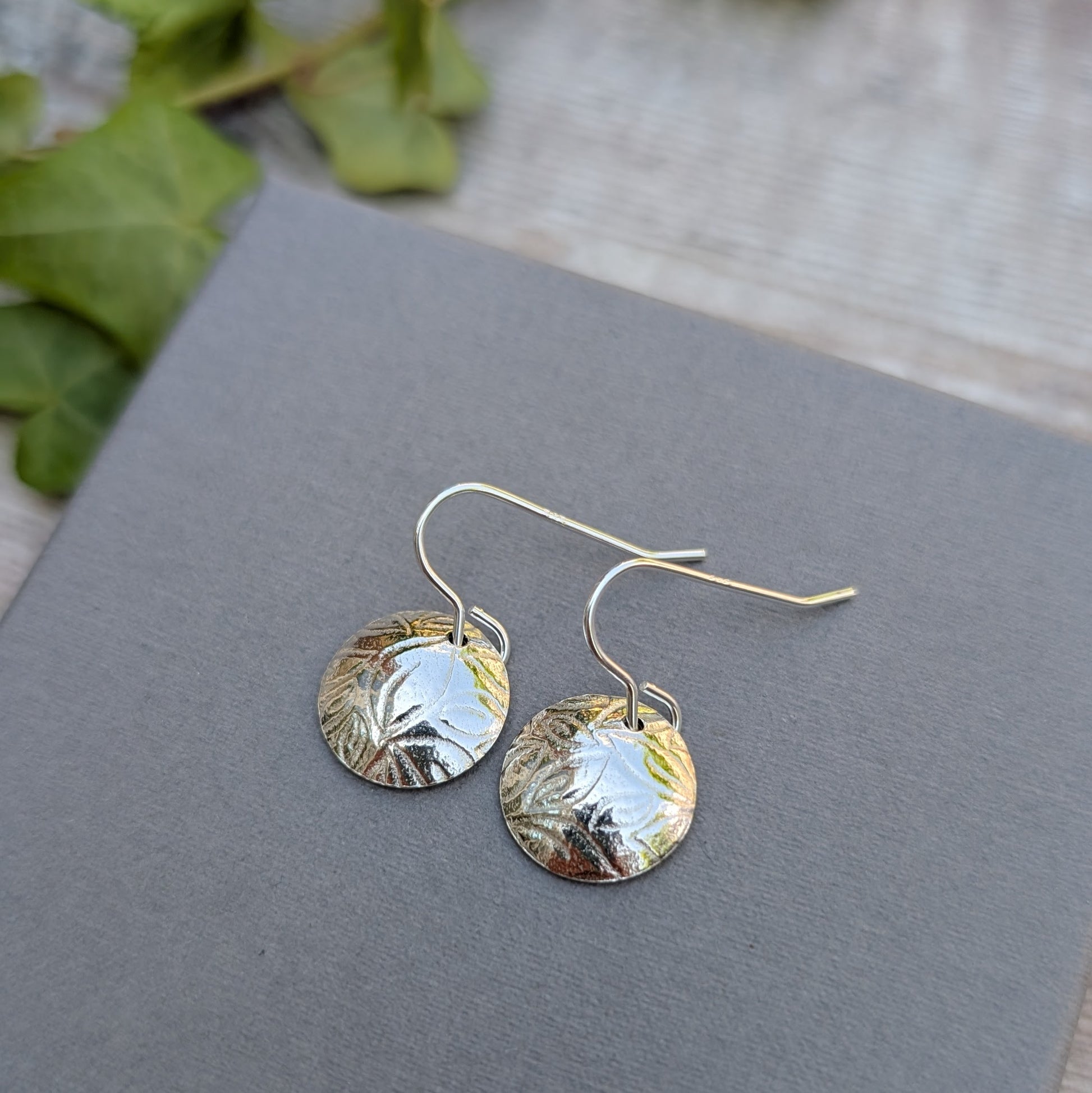 Silver Dome Disc Earrings with Leaf Pattern displayed on a grey surface with natural light.