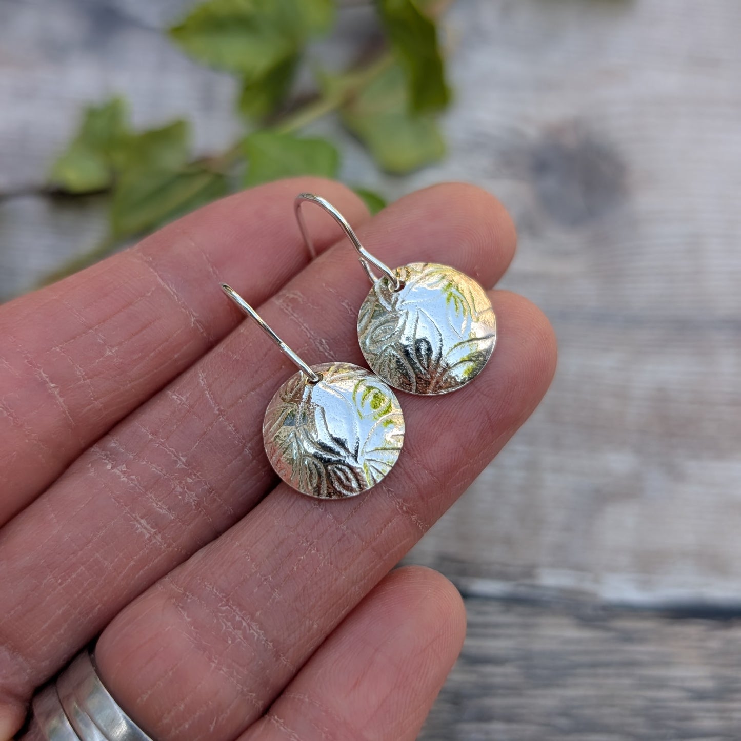 Close-up of Silver Dome Disc Earrings with Leaf Pattern held in hand, showing the pressed leaf detail.