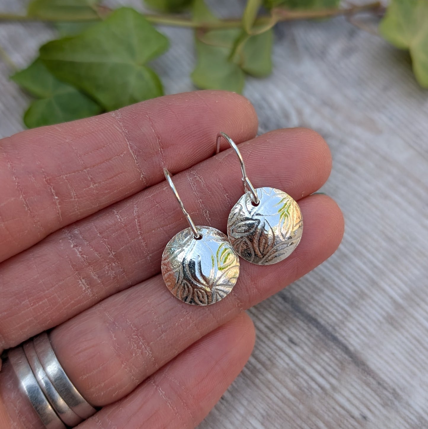 Detailed view of Silver Dome Disc Earrings with Leaf Pattern in hand, highlighting texture and shine.