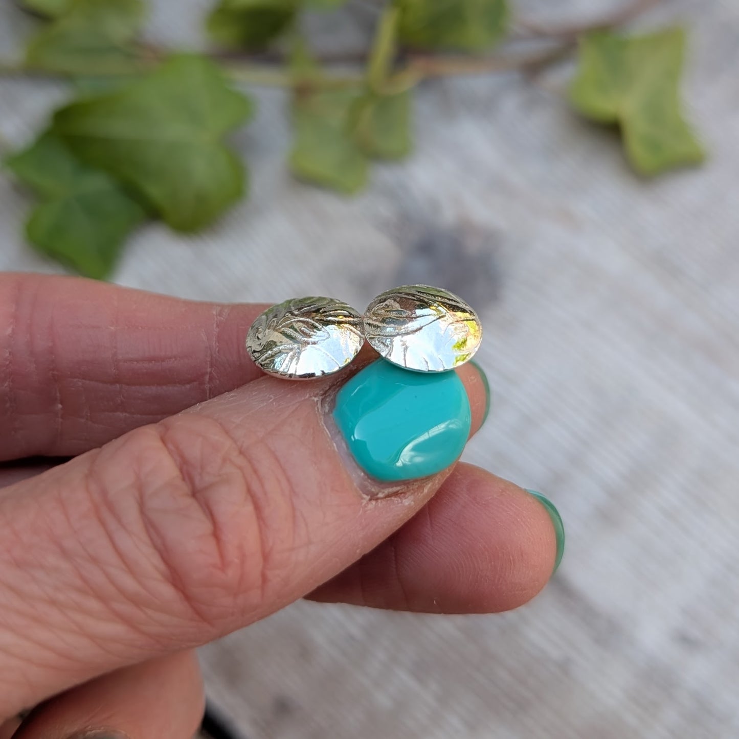 Silver Dome Disc Stud Earrings with Leaf Pattern held between fingers, showing the domed shape and pressed leaf design in recycled sterling silver.