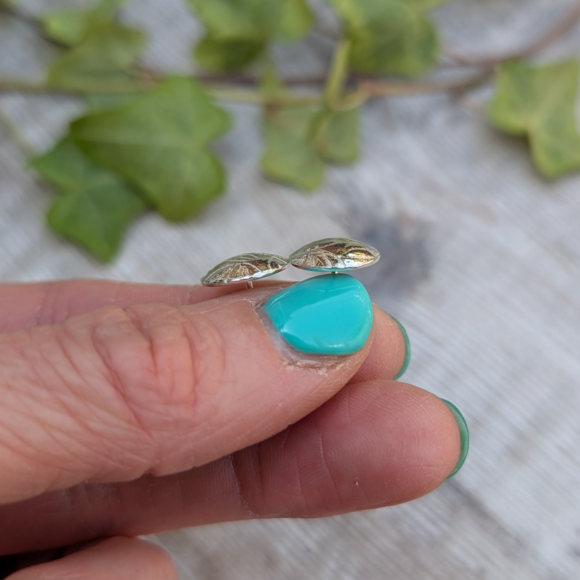 Side view of Silver Dome Disc Stud Earrings with Leaf Pattern resting on a fingertip, showing the gentle dome and stud post.