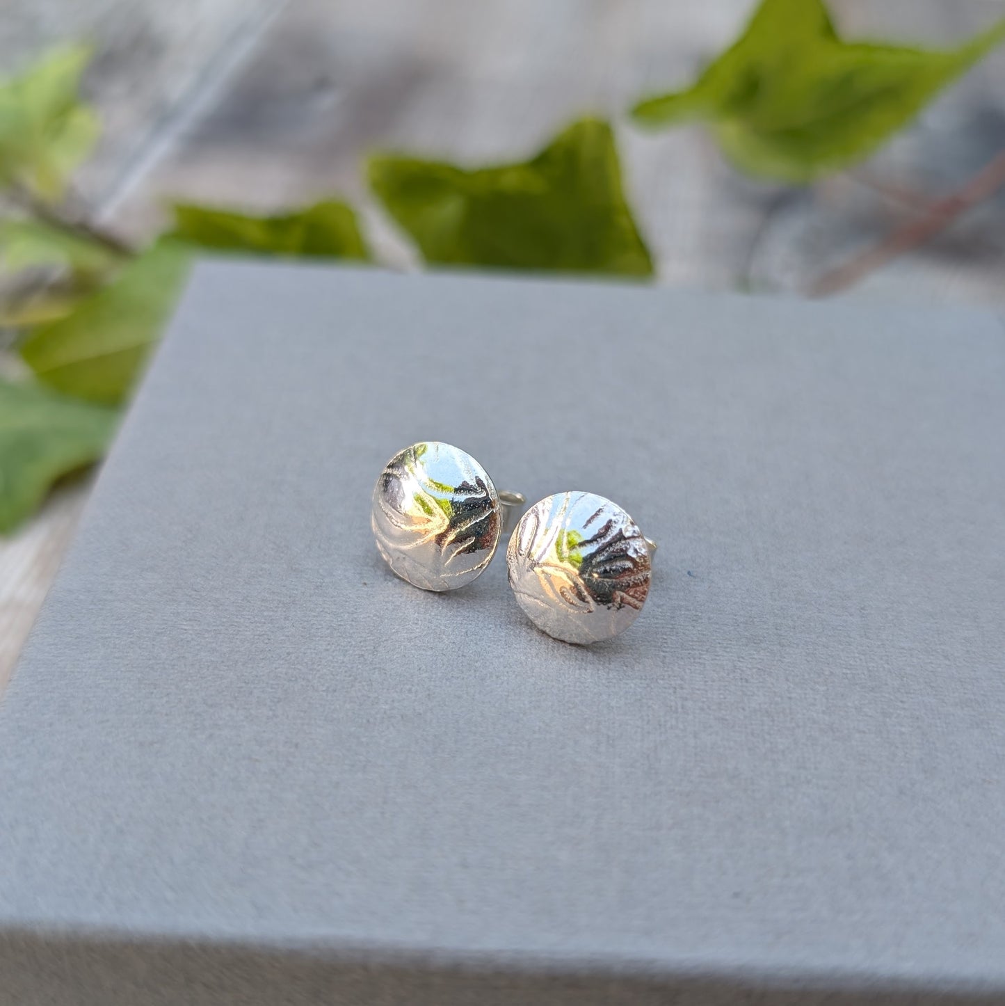 Silver Dome Disc Stud Earrings with Leaf Pattern on a display box, showing both earrings side by side in natural light.