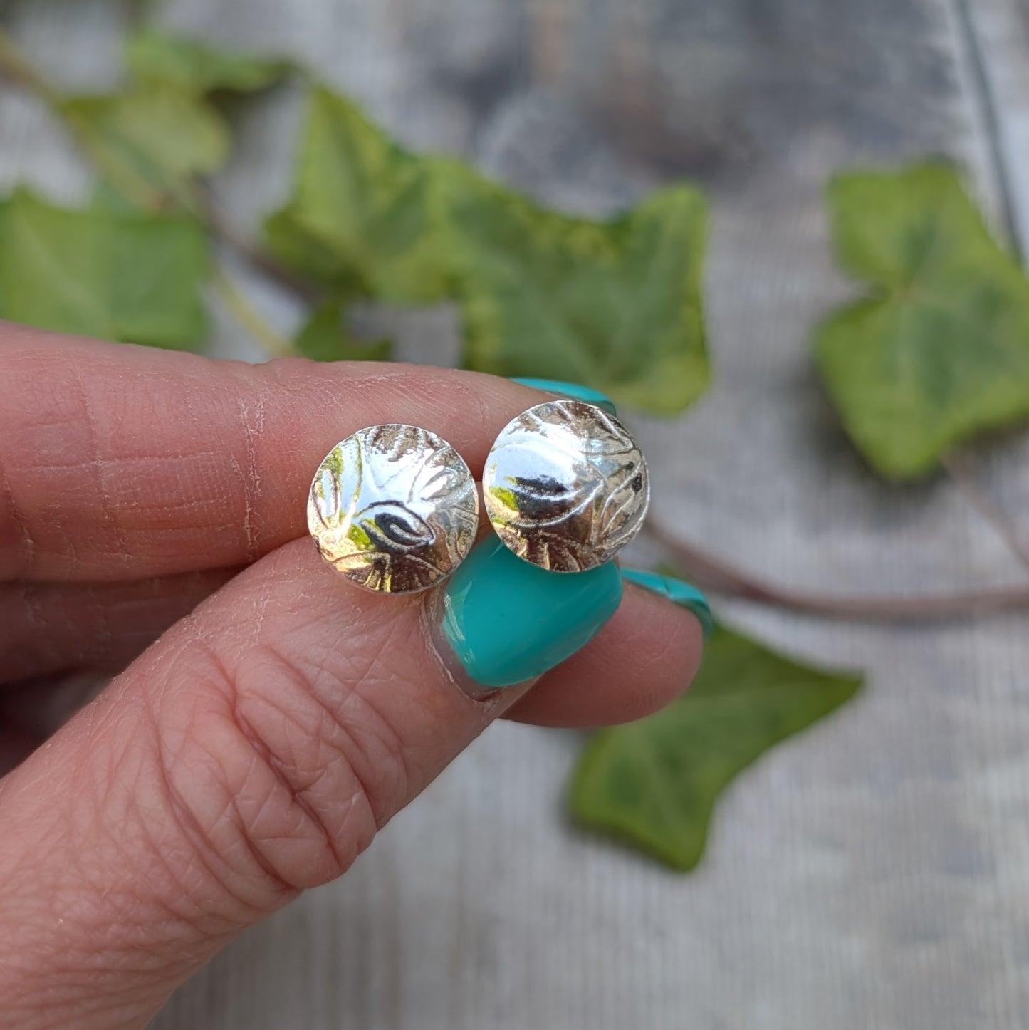 Silver Dome Disc Stud Earrings with Leaf Pattern held in hand, showing the reflective surface and detailed leaf pattern.