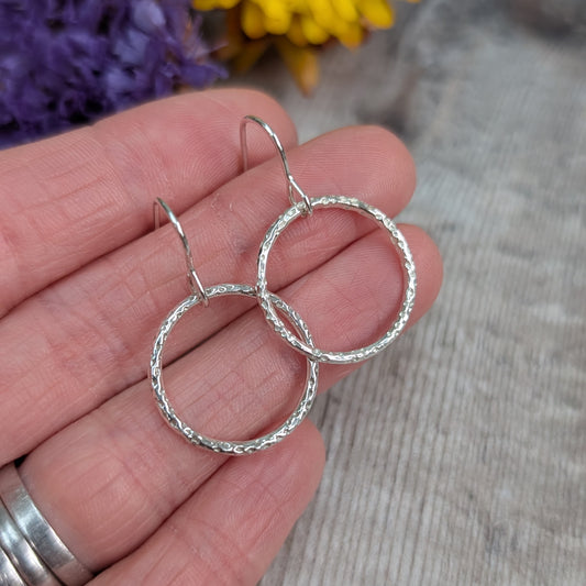 Hand holding Silver Dot Textured Circle Earrings close up, showing the detailed dotted pattern and circular shape.