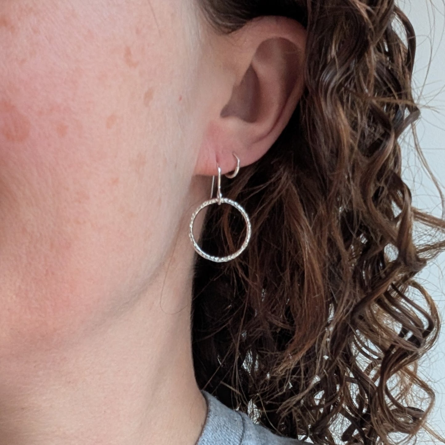 Silver Dot Textured Circle Earrings worn on an ear, showing their lightweight design and subtle shimmer.