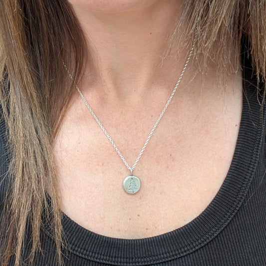 Silver evergreen tree pebble necklace being worn, showing the small circular pendant on a fine silver chain.
