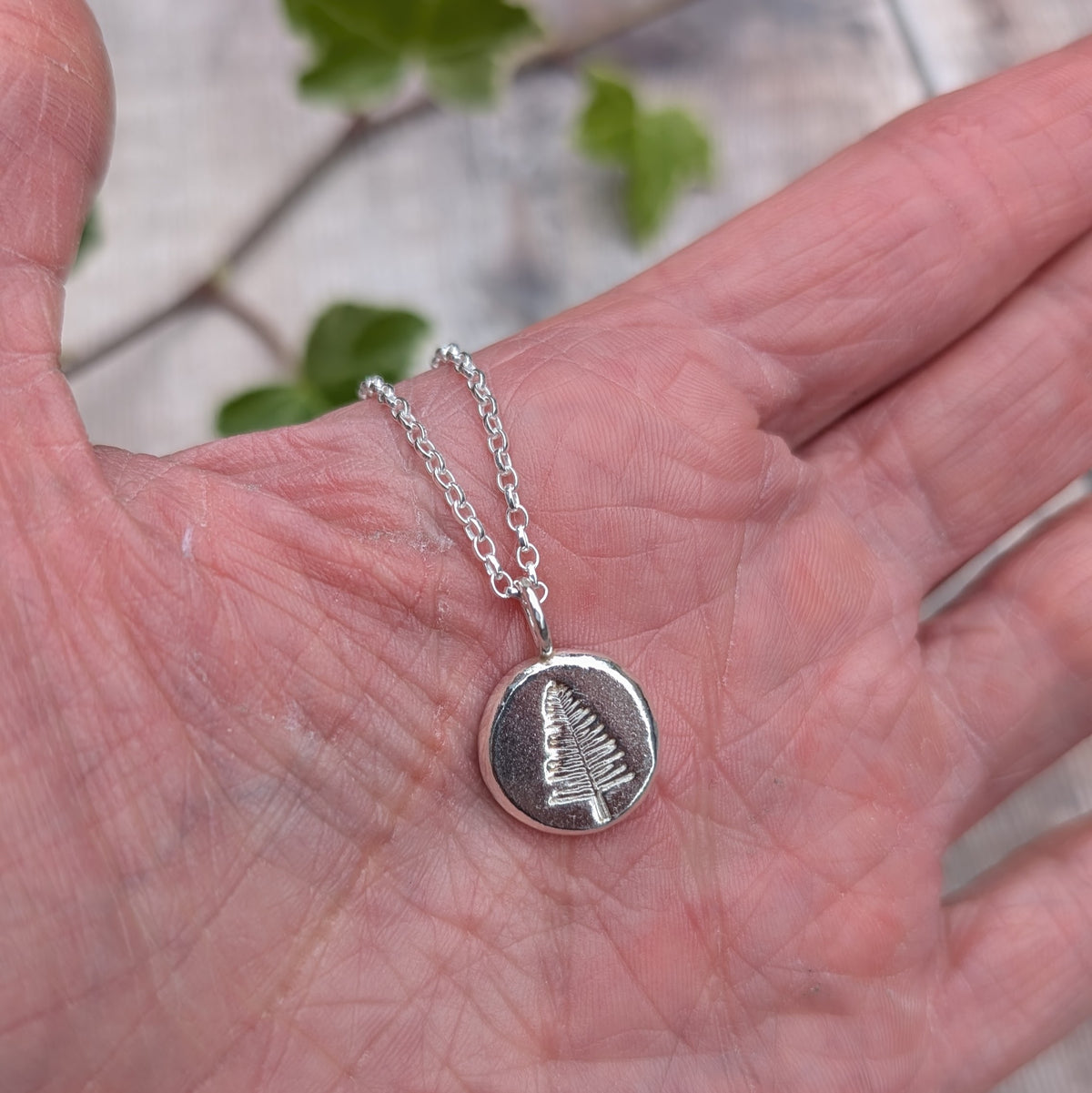 Handmade silver evergreen tree necklace with a stamped evergreen tree pendant displayed on a grey background.