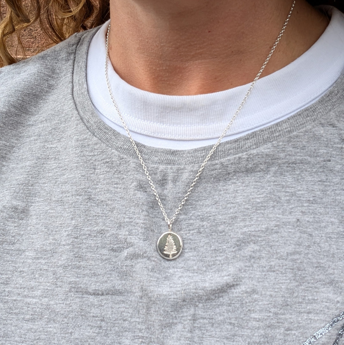 Silver evergreen tree necklace shown in a hand to show the size of the round recycled Sterling Silver pendant.
