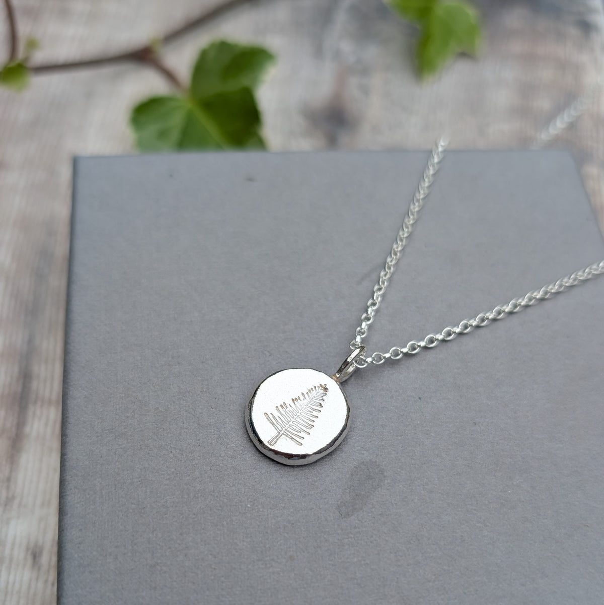 Close up of a silver evergreen tree necklace with a hand stamped evergreen tree design on a round silver pendant.