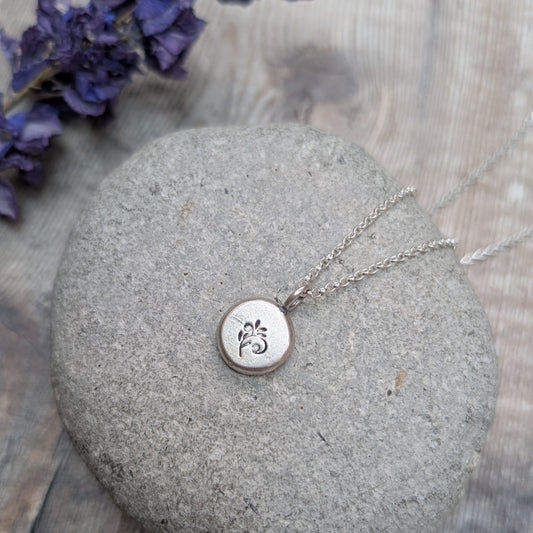 Silver flower pebble necklace resting on a smooth grey stone with purple flowers in the background.
