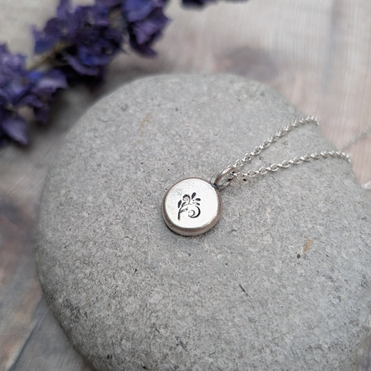 Close-up of a silver flower pebble necklace on a stone, showing the small stamped flower design.