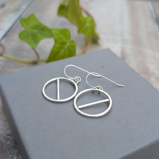 Handmade silver geometric circle earrings with straight bar detail, displayed on a grey jewellery box with ivy in the background.