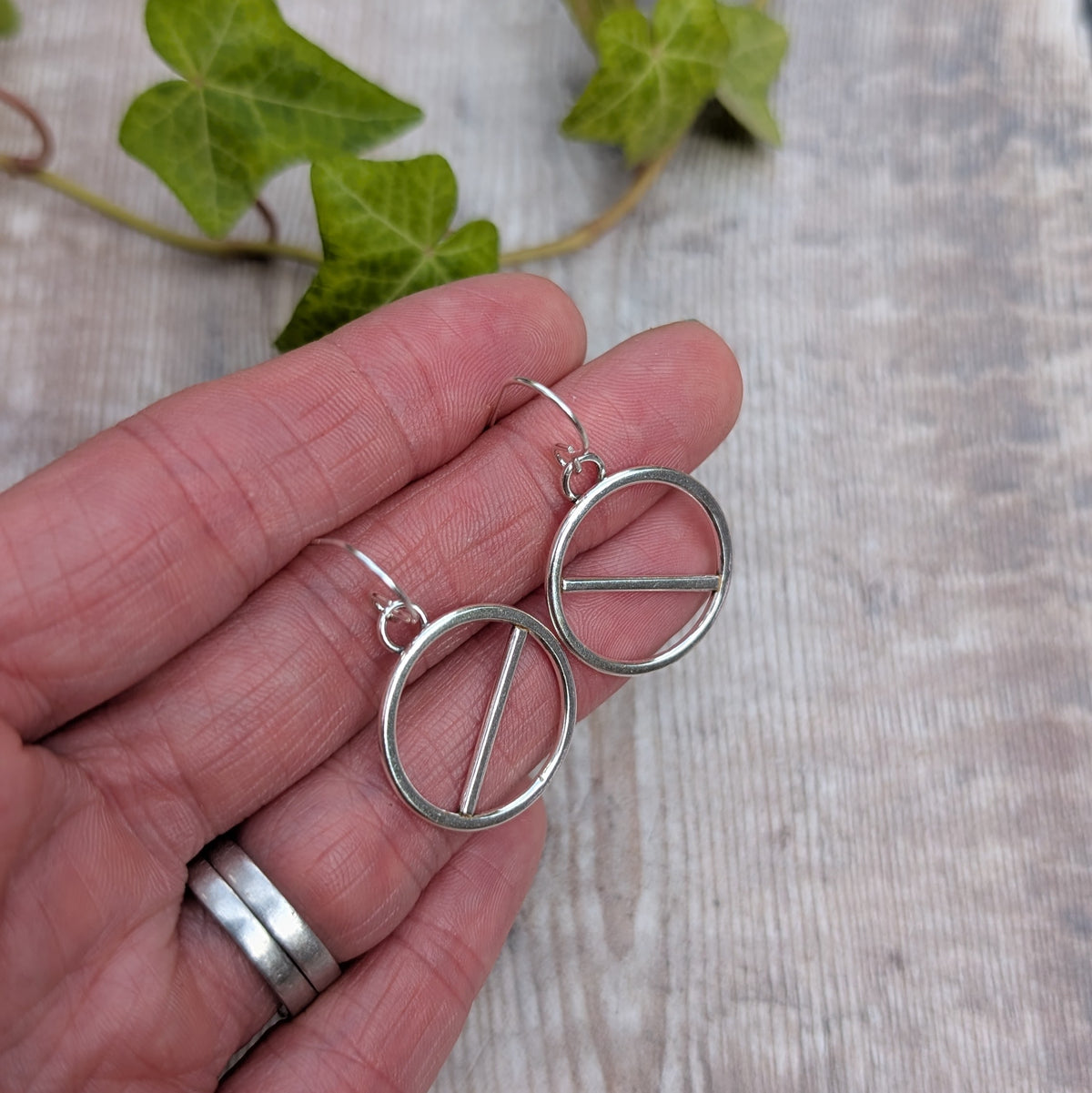 Back view of silver geometric circle earrings held in a hand, showing the circle, straight bar design and silver ear wires.