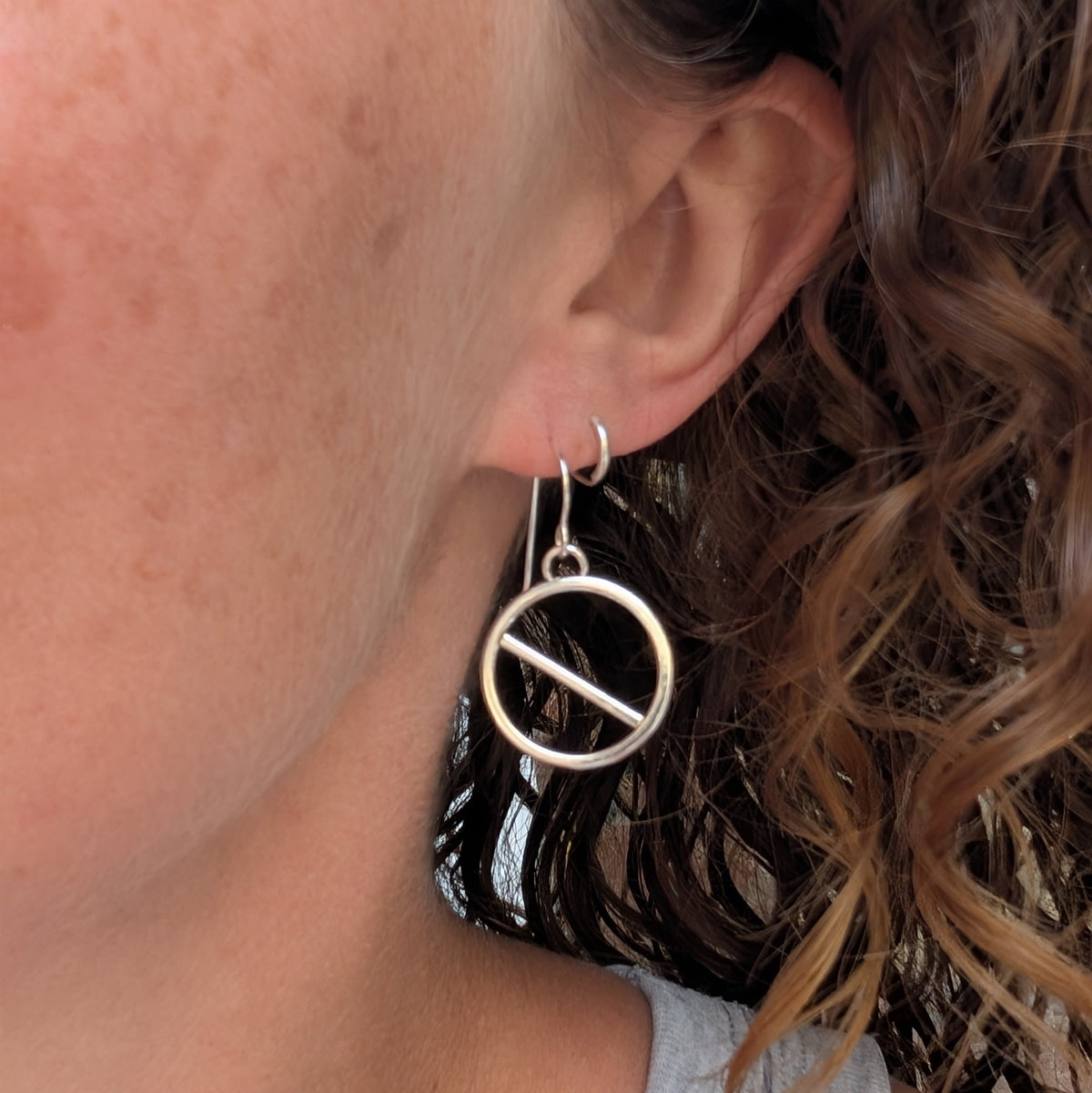 Silver geometric circle earrings being worn, showing the size and drop of the handmade circular design.