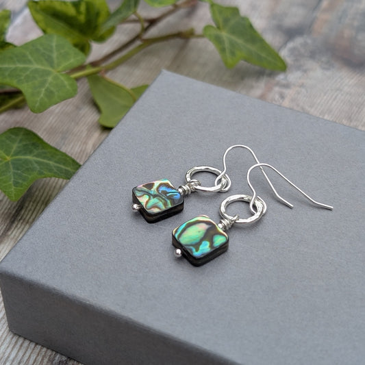 Silver Hammered Circle Earrings with Abalone Shell Beads laid on a grey surface with soft natural lighting