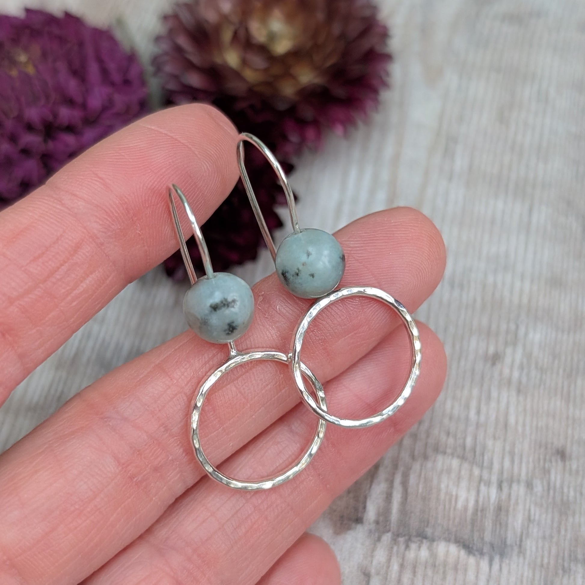 Close-up of Silver Hammered Circle Earrings with Kiwi Jasper held between fingers, highlighting the smooth round stones and reflective hammered finish.