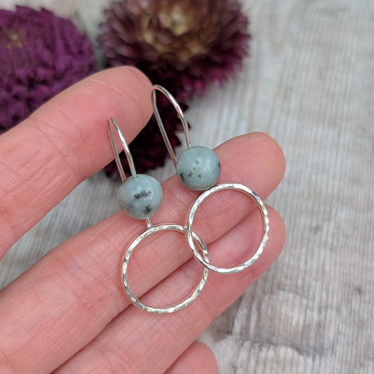 Close-up of Silver Hammered Circle Earrings with Kiwi Jasper held between fingers, highlighting the smooth round stones and reflective hammered finish.