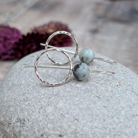 Silver Hammered Circle Earrings with Kiwi Jasper resting on a smooth grey stone, showing the hammered silver circles and natural stone beads.