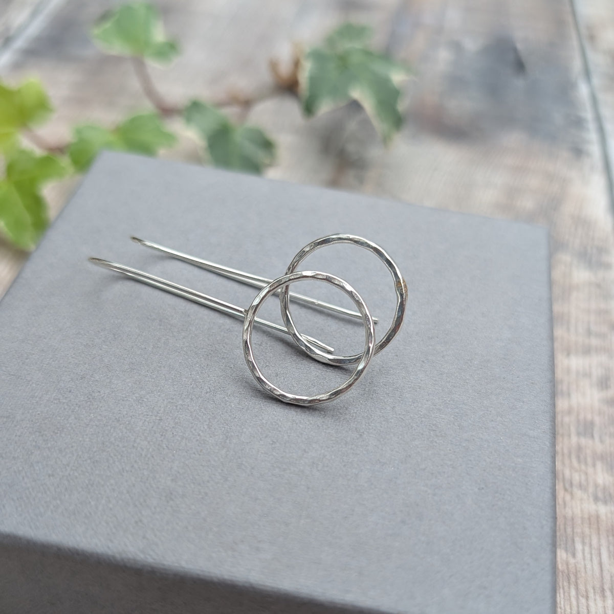 Pair of silver hammered circle long earrings lying on a pale grey jewellery box, showing the hammered silver circles and long handmade ear wires.