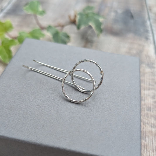 Pair of silver hammered circle long earrings lying on a pale grey jewellery box, showing the hammered silver circles and long handmade ear wires.