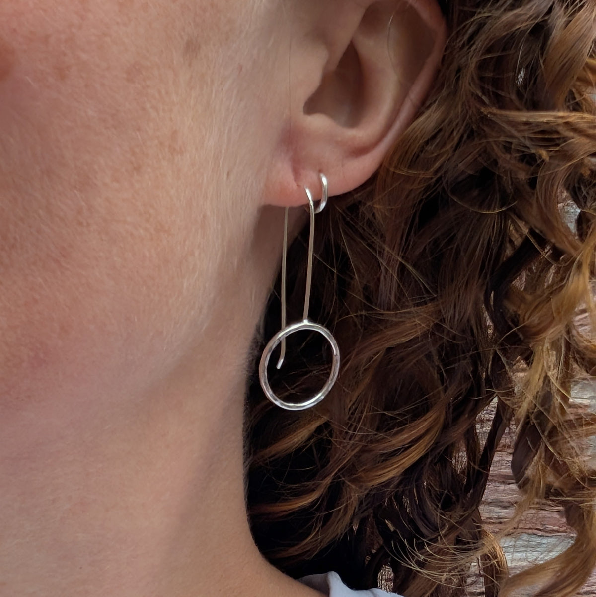 Silver hammered circle long earrings being worn, showing how the open silver circles hang below the earlobe from long silver ear wires.
