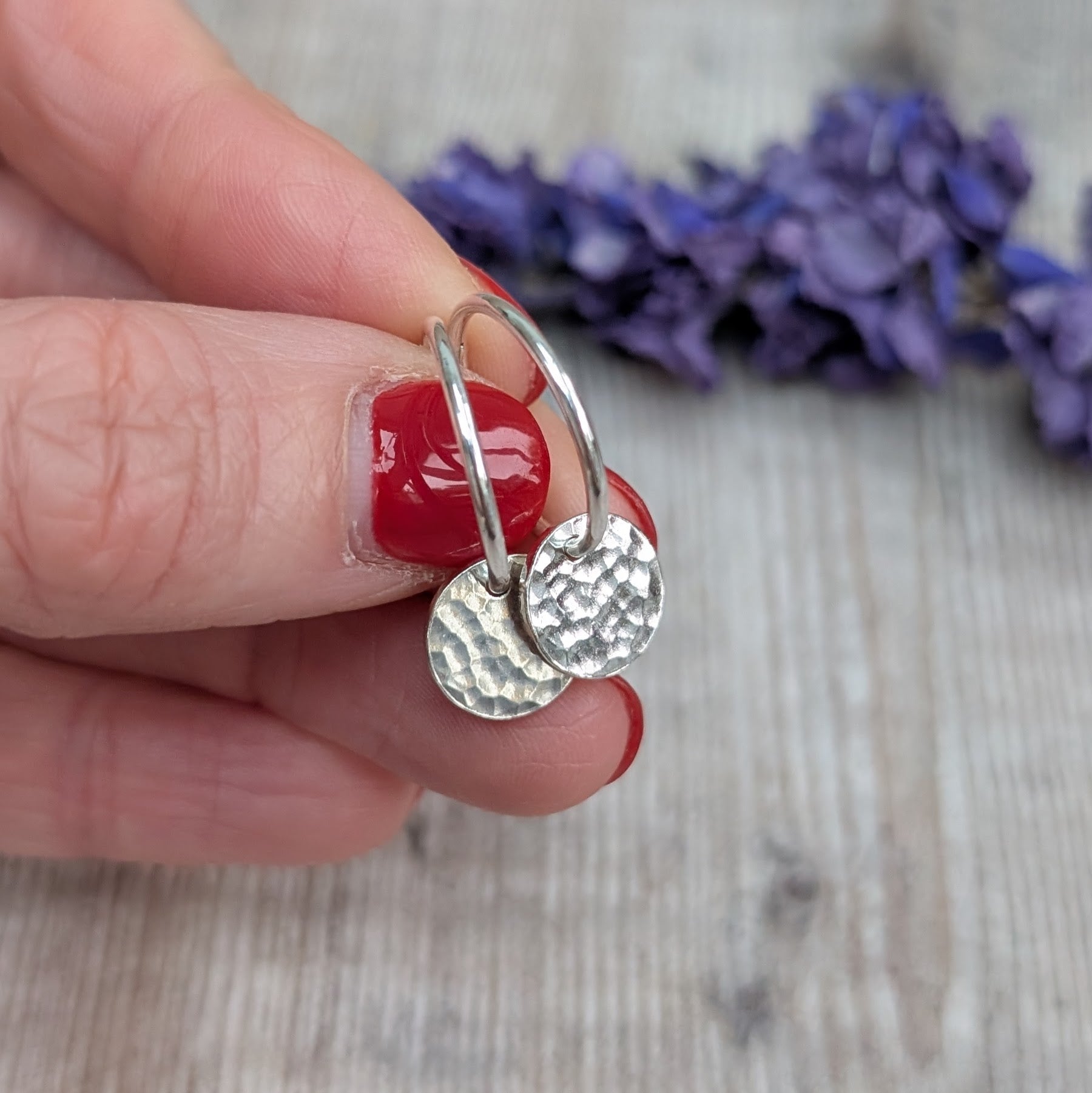 Hand holding Silver Hammered Disc Hoop Earrings close up, showing the reflective hammered surface and minimalist hoop design.