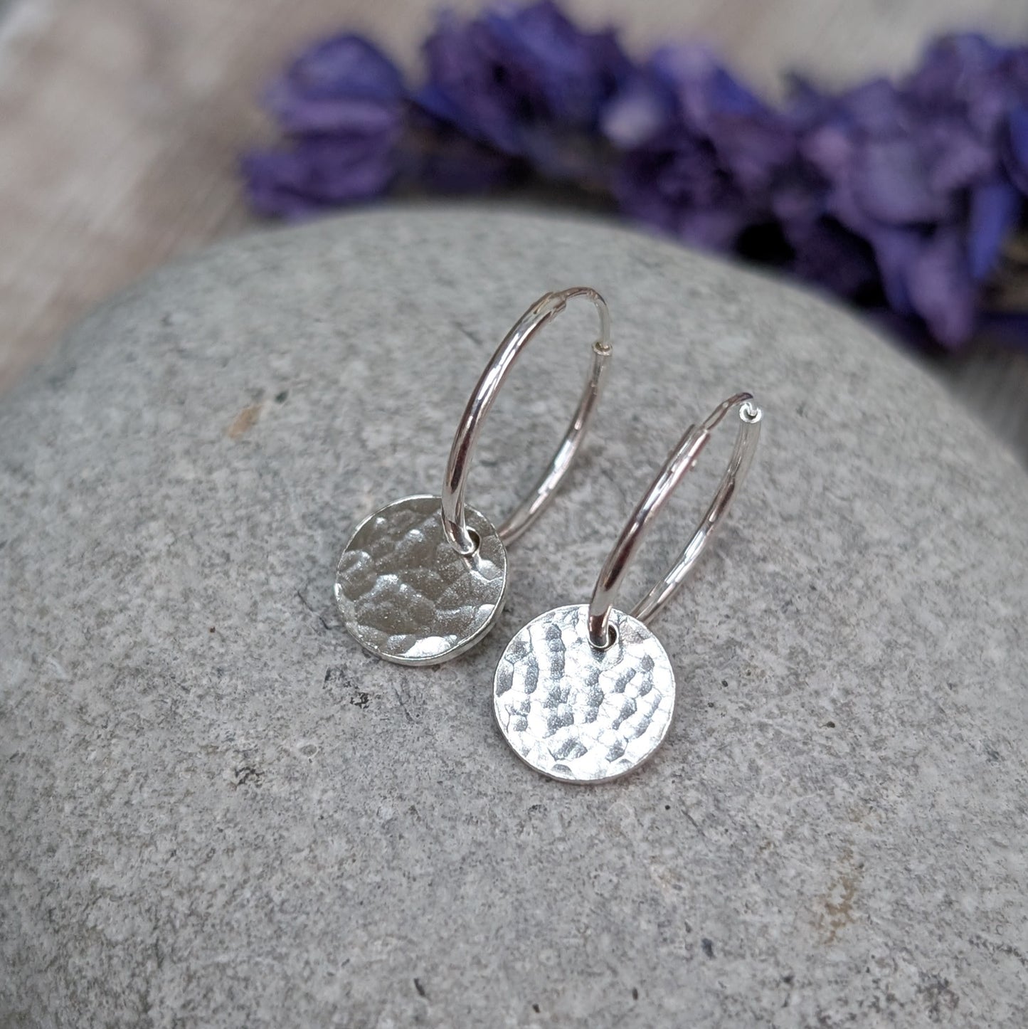 Close-up of Silver Hammered Disc Hoop Earrings on a grey stone, highlighting the lightly hammered texture that catches the light.