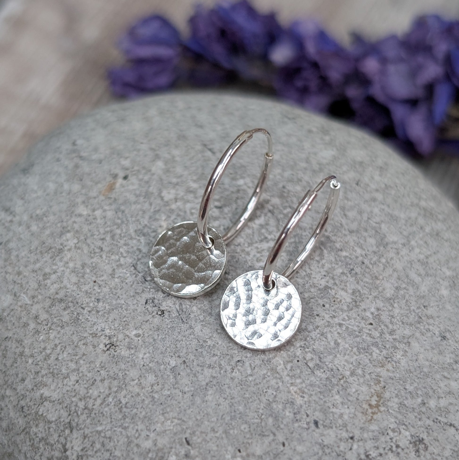 Close-up of Silver Hammered Disc Hoop Earrings on a grey stone, highlighting the lightly hammered texture that catches the light.