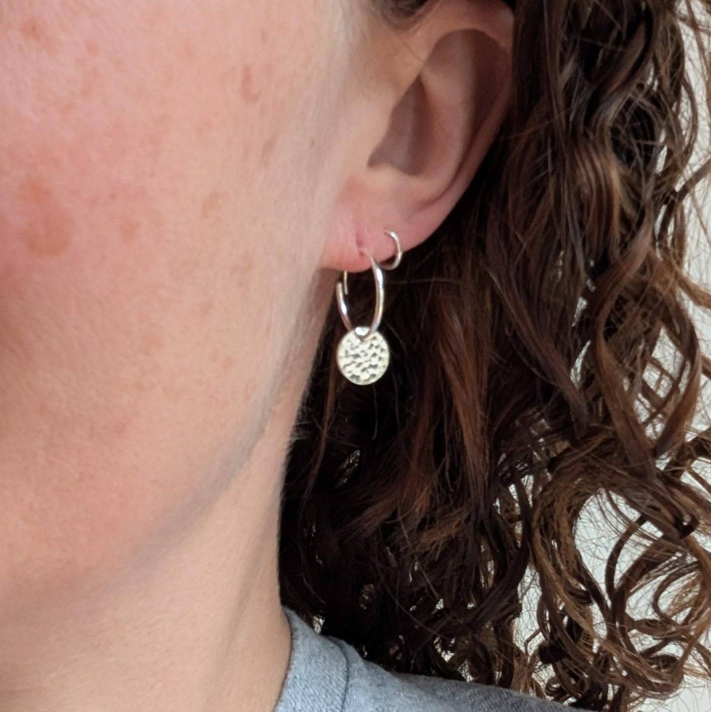 Silver Hammered Disc Hoop Earrings worn on an ear, showing their comfortable size and gentle movement when worn.