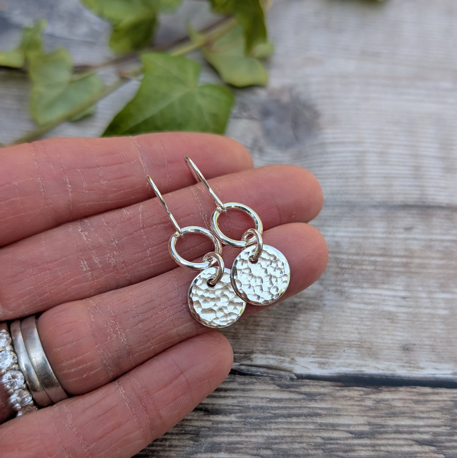 Small Silver hammered disc and circle earrings handmade from recycled Sterling Silver shown resting on a hand to highlight their size and detail.
