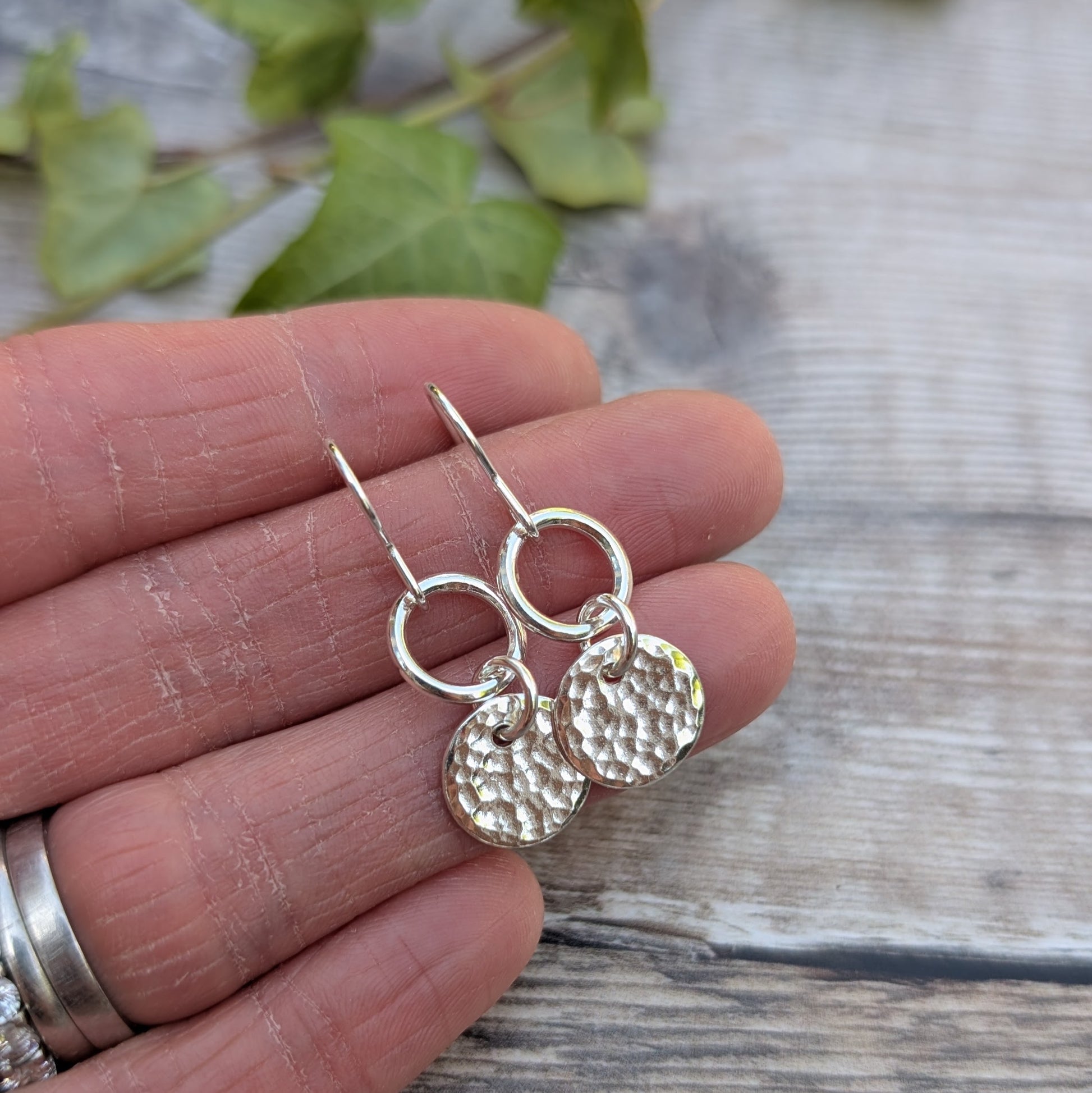 Silver hammered disc and circle earrings handmade from recycled Sterling Silver displayed on a hand, featuring shiny hammered discs and circular links.