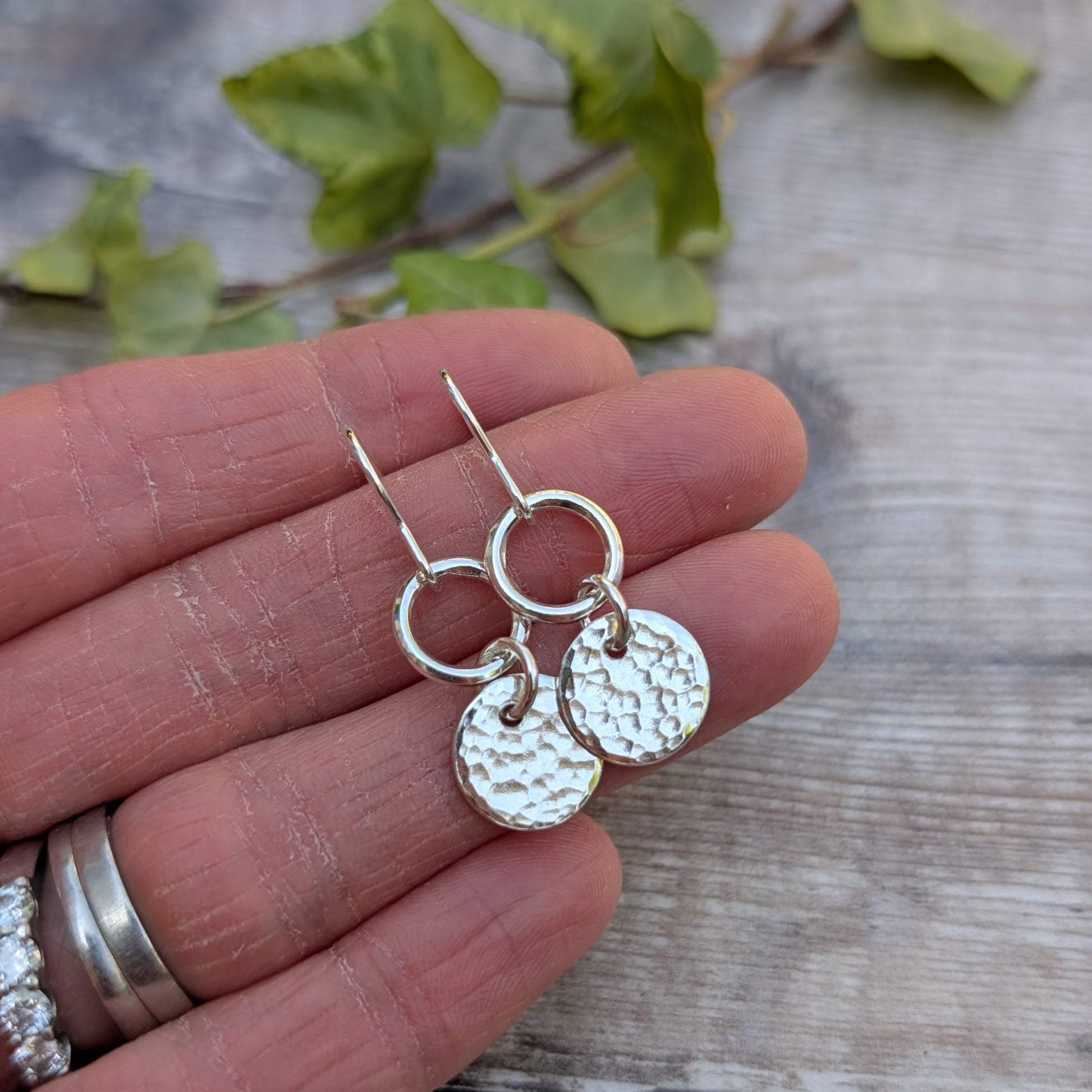 Handmade Silver hammered disc and circle earrings in recycled Sterling Silver shown close-up on a hand, highlighting the hammered surface pattern and polished circles.