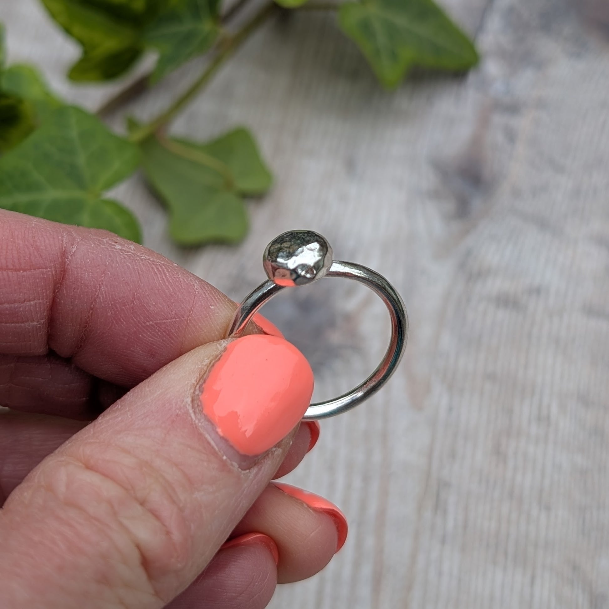 Silver Hammered Pebble Ring held up against a soft background, showing the simple band and pebble top