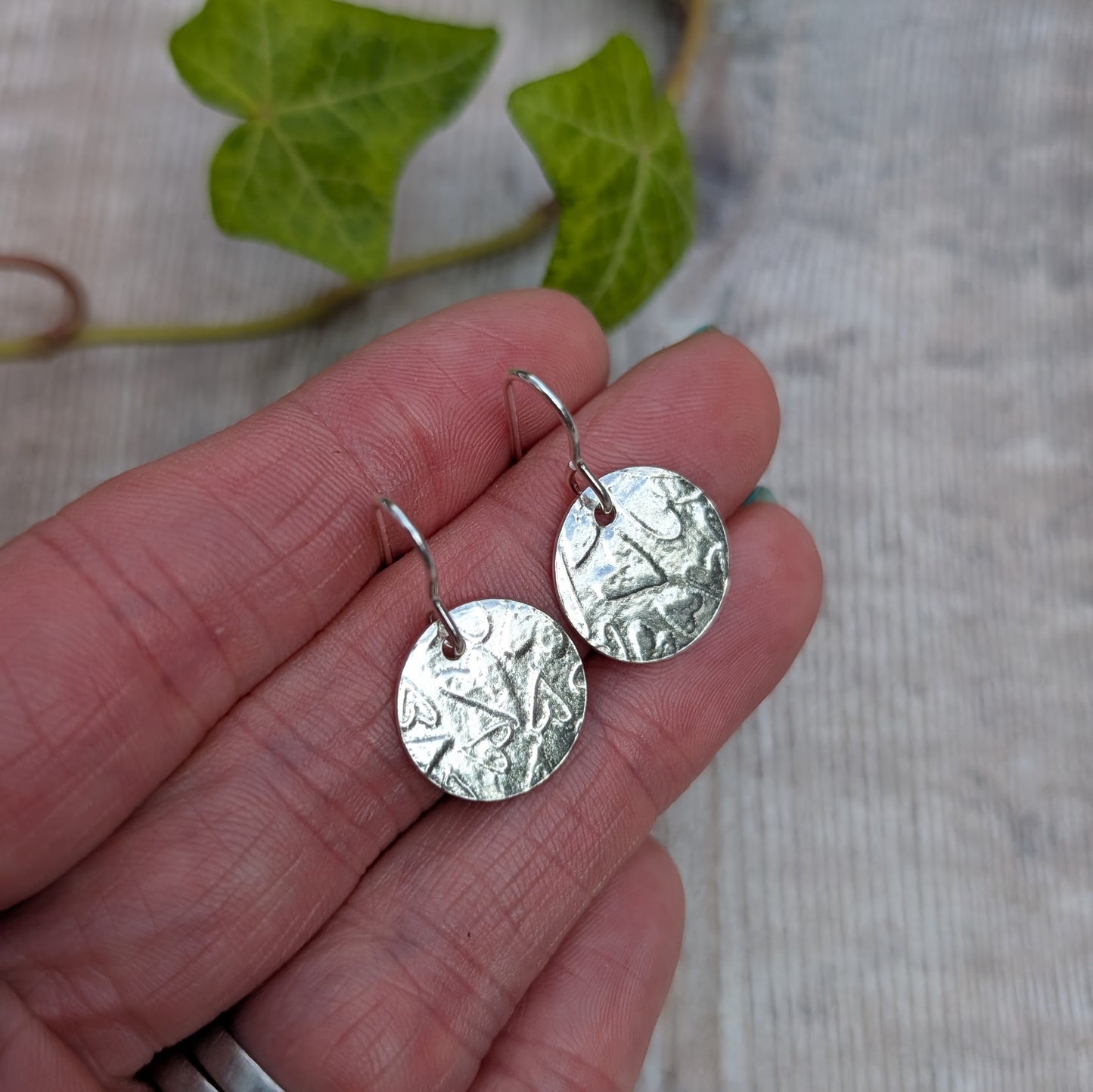 Silver heart pattern disc earrings handmade from recycled Sterling Silver, held in a hand to show the heart patterned round discs.