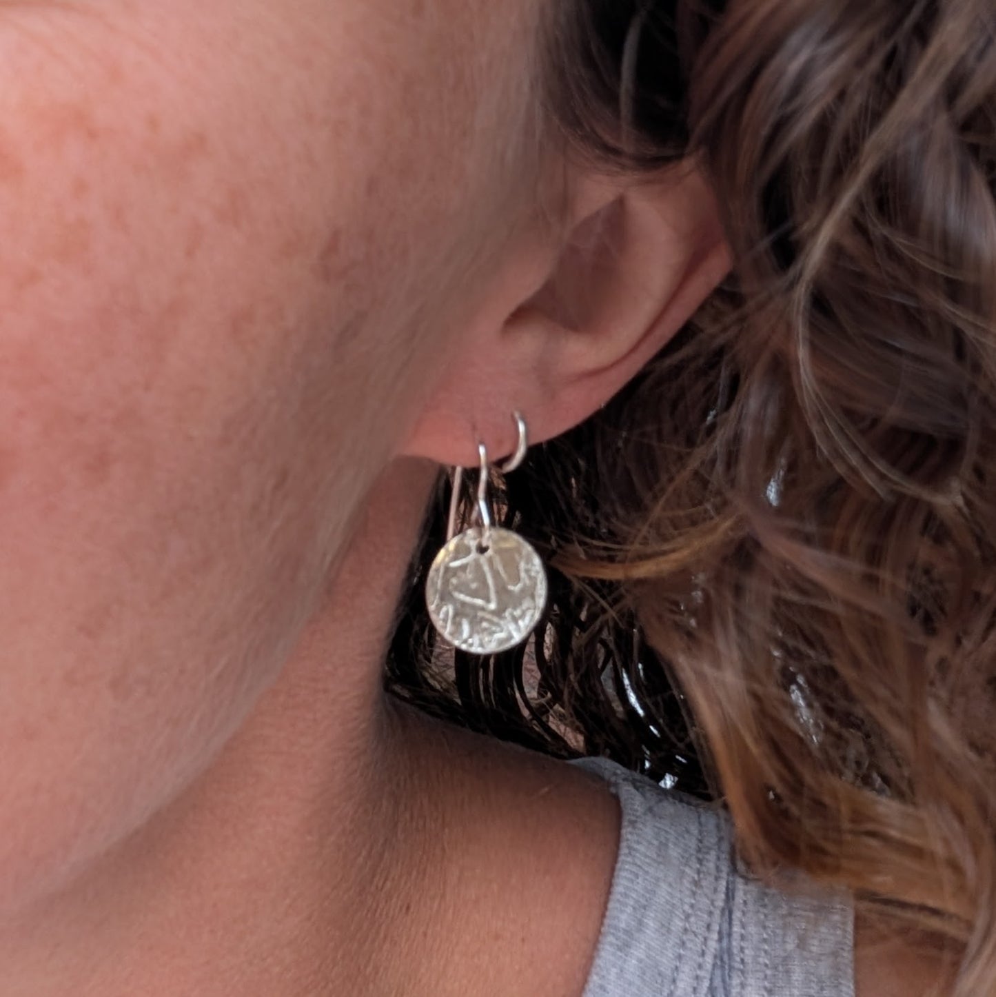 Silver heart pattern disc earrings handmade from recycled Sterling Silver, shown being worn to give an idea of their size and drop.