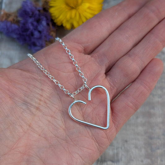 Silver heart ring keeper necklace held in the palm of a hand, showing the open heart shape on its chain.