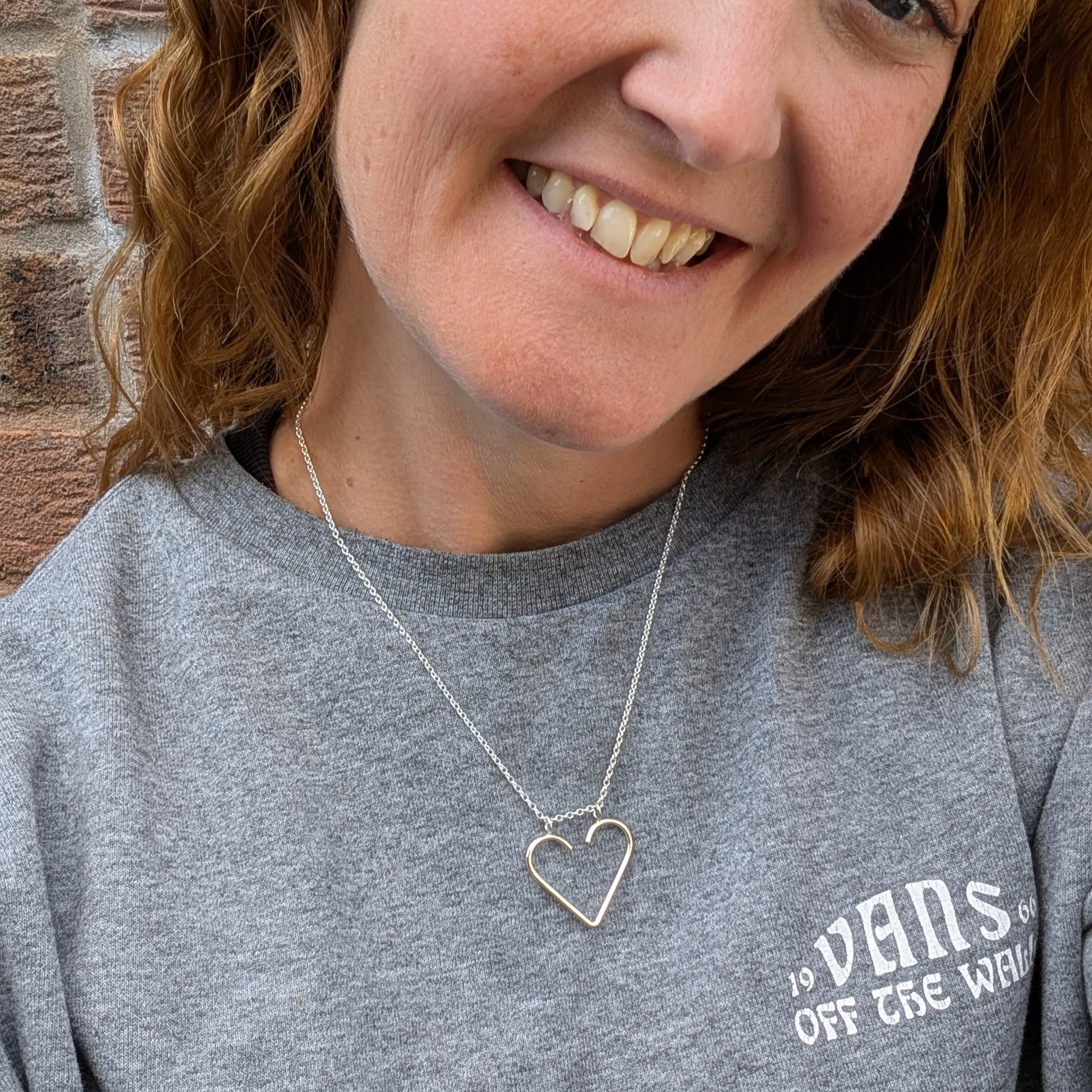 Woman wearing the silver heart ring keeper necklace with a grey t-shirt, the heart pendant resting at the collarbone.