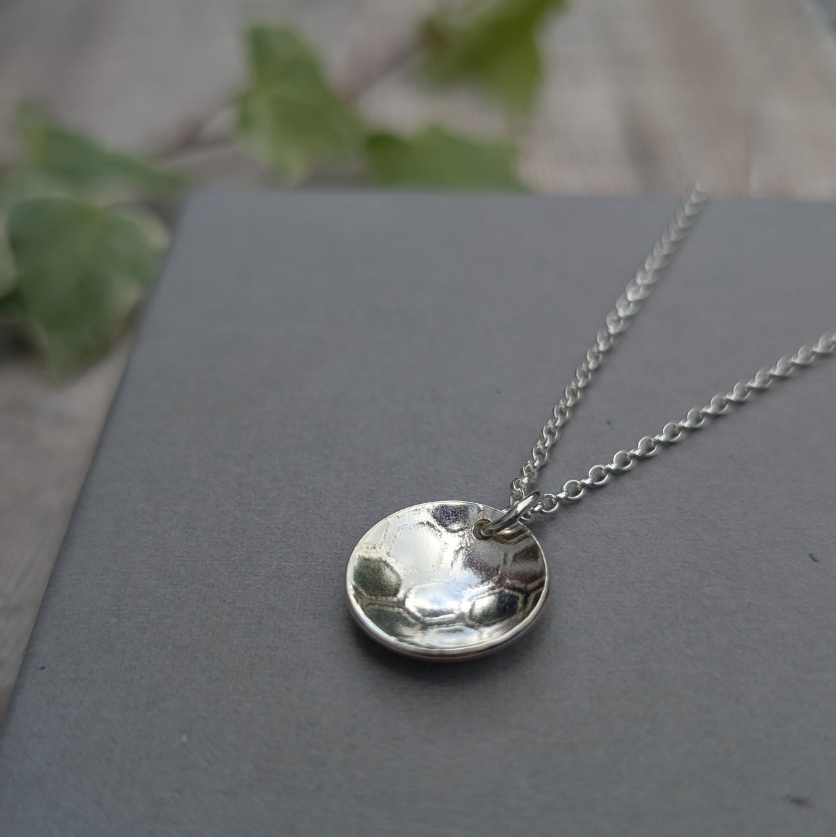 Close up of a silver honeycomb disc necklace showing the curved silver pendant and textured honeycomb pattern.