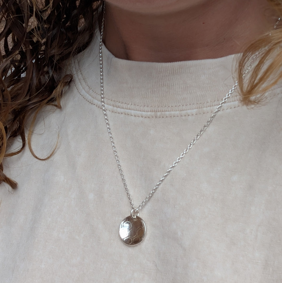 Silver honeycomb disc necklace being worn, showing the size and length of the round patterned pendant.
