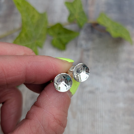 Close up of silver honeycomb disc stud earrings held between fingers, showing the honeycomb pattern pressed into the recycled Sterling Silver.