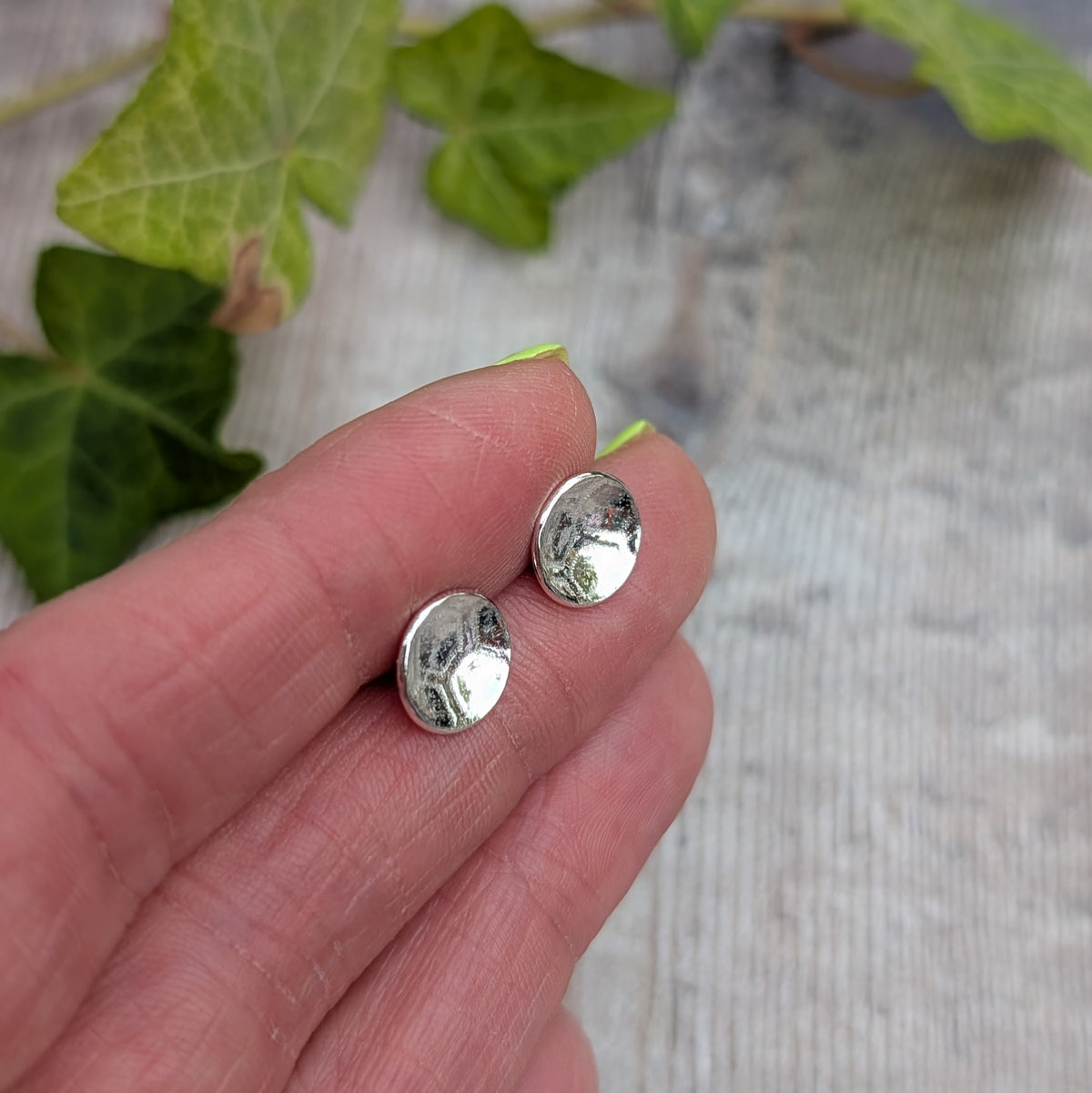Silver honeycomb disc stud earrings held on fingertips, showing the pressed honeycomb pattern and round disc shape.
