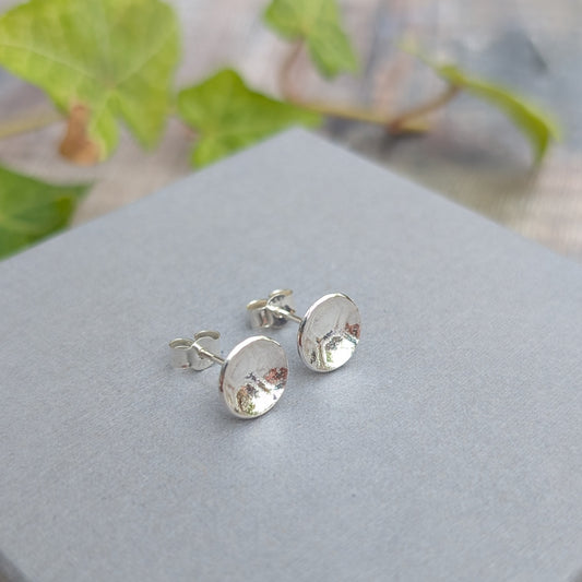 Silver honeycomb disc stud earrings displayed on a grey surface, showing the patterned silver discs, posts and butterfly backs.