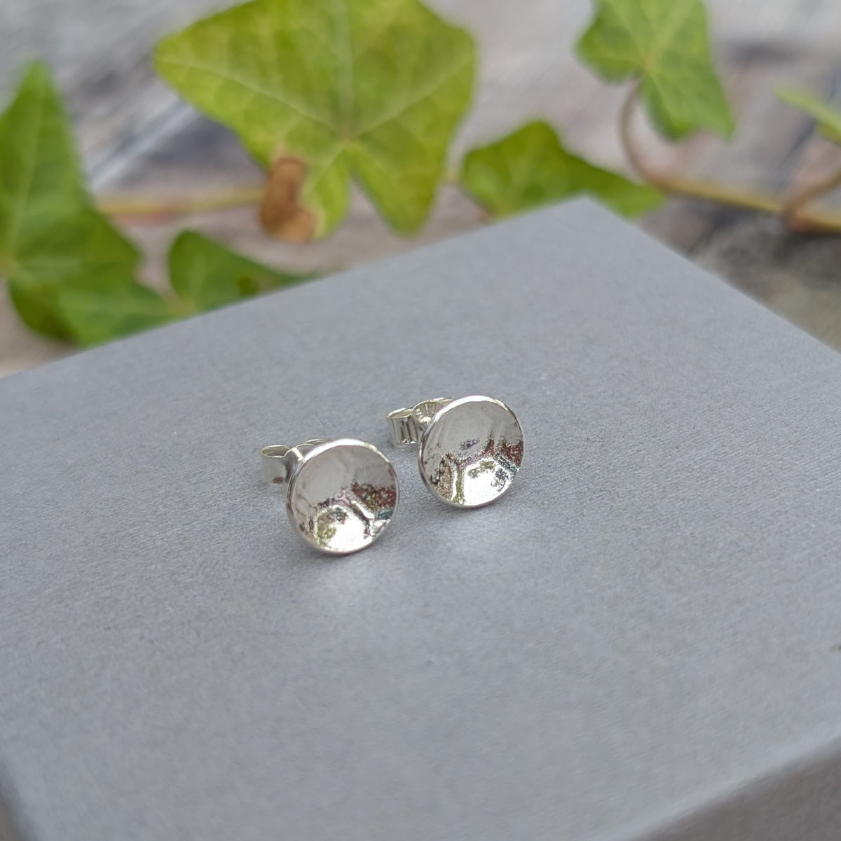 Silver honeycomb disc stud earrings handmade from recycled Sterling Silver, displayed together on a grey surface with ivy in the background.
